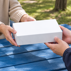 Lukket hvid kageæske bæres ved blåt picnicbord