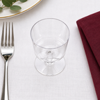 Klart vinglas på kort fast fod set ovenfra ved kuvert med bordeaux serviet, stemningsillustration