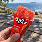 Nærbillede af åbnet Sun Lolly Jordbær-is med havet i baggrunden