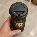 Sort låg på Beans-kaffebæger med gylden bønne holdt i hånden