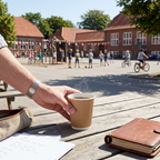 Voksen sætter kaffebæger på bord ved solrig skolegård