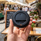 Voksen holder et løst sort drikkelåg ved solrig markedscafé