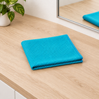 Foldet blåt mikrofiberviskestykke 40 × 70 cm ved spejl og træbord