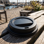 Sort drikkelåg på træbænk ved solrig havneterrasse