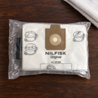 Miljøbillede af Nilfisk-fleeceposer i emballage på mørkt træbord