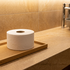 Hvid Tork Mini Jumbo-toiletrulle på træbakke i varmt belyst toiletmiljø