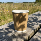 Brunt kaffebæger på træbord med åbent grønt landskab i solskin