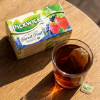 Pickwick Skovbær-teæske ved et glas mørk te på solbelyst træbord; glas medfølger ikke