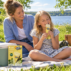 Barn og forælder med Sun Lolly Hyldeblomst på picnictæppe ved sø