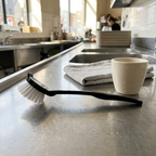 Basic-opvaskebørste ved kop og separat håndklæde i caféens opvaskeområde, stemningsbillede
